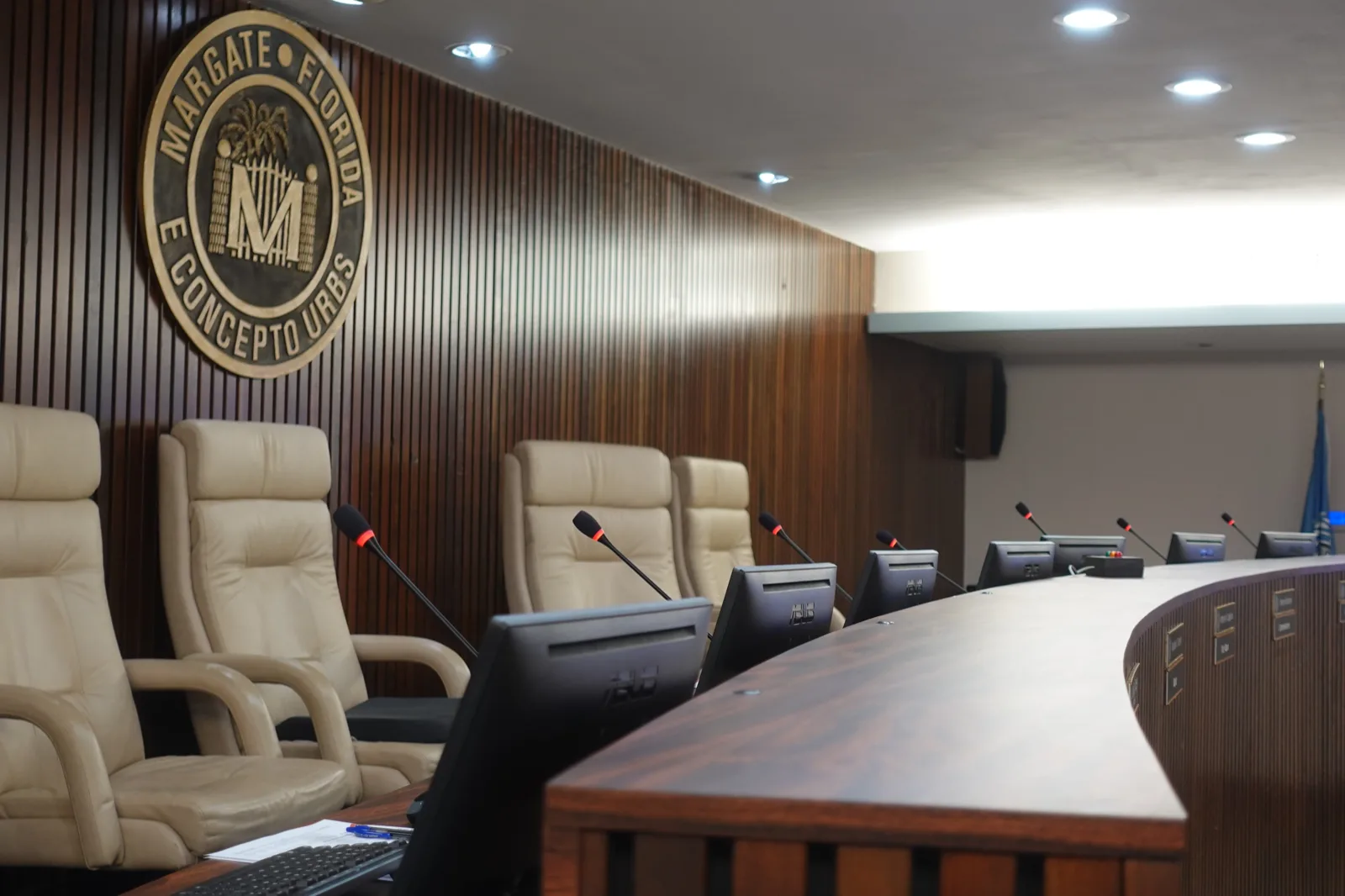 The City of Margate, Florida council chamber dais with the city seal on the wood-panel wall, gooseneck microphones and dais monitors at each seat, in a chamber supported by Full Moon Creative government AV